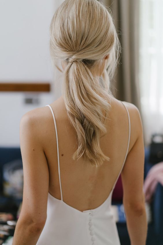 a simple low ponytail with twists and waves plus a volume on top is a cool idea for a modern or minimalist bride