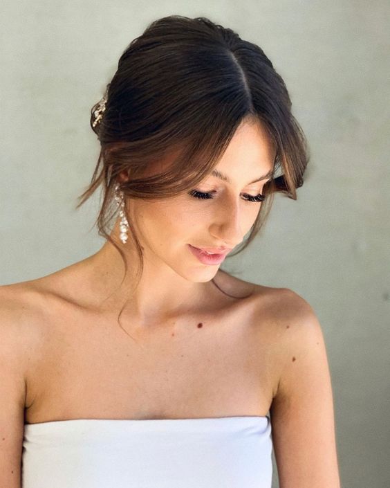 a simple low updo with long curtain bangs and central parting are a lovely and effortless idea for a wedding