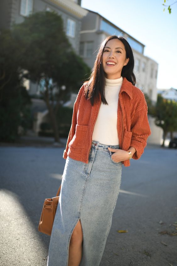 a spring or fall outfit with a white turtleneck, a blue denim maxi, an orange corduroy blazer and a brown bag