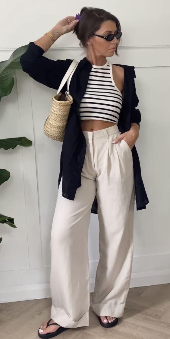 a spring outfit with a striped top, a black button down, neutral trousers, black flipflops and a woven bag