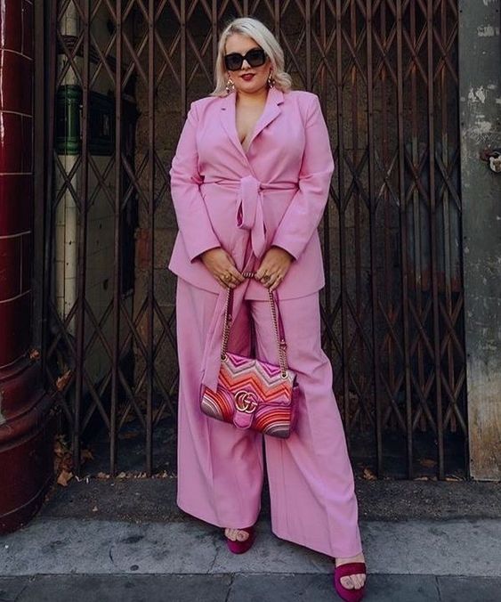 a spring wedding guest look with a pink pantsuit with a sash, burgundy shoes, a striped chevron bag and statement earrings