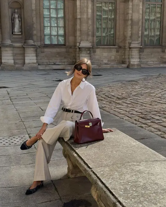 a stylish old money work look with a white button down, light grey pants, black slingbacks and a burgundy bag