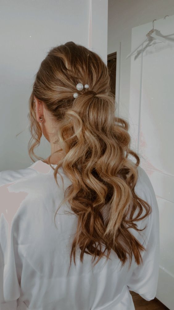 A super cool wavy low ponytail with a volume on top and face framing hair plus some pearl hair pins is a cool idea for a modern bride