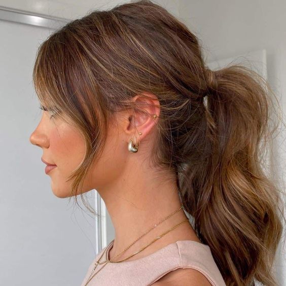 a volumetric and wavy midi ponytail with a bump on top and hair framing the face is a cool and chic casual wedding hairstyle