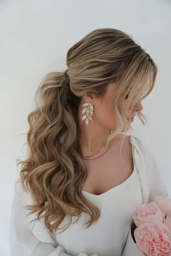 A voluminous wavy ponytail with a bump on top and face framing hair is adorable for most bridal styles