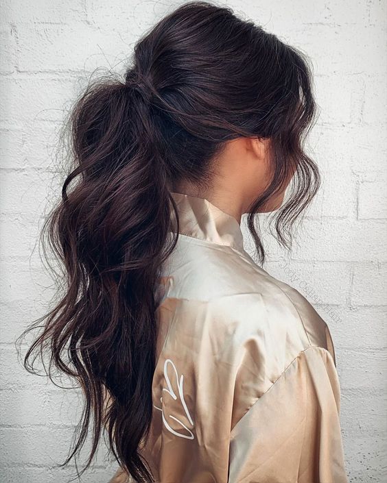 a wavy and volumetric low ponytail with a bump on top and face-framing hair is a cool messy hairstyle for a casual wedding