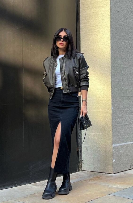 a white tee, a black denim maxi skirt, a brown cropped leather jacket, black boots and a small bag
