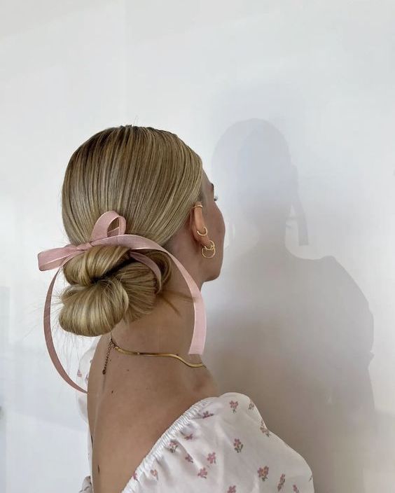 a woven low bun with a sleek top and a small pink ribbon bow are a lovely and chic idea for a cute girlish look