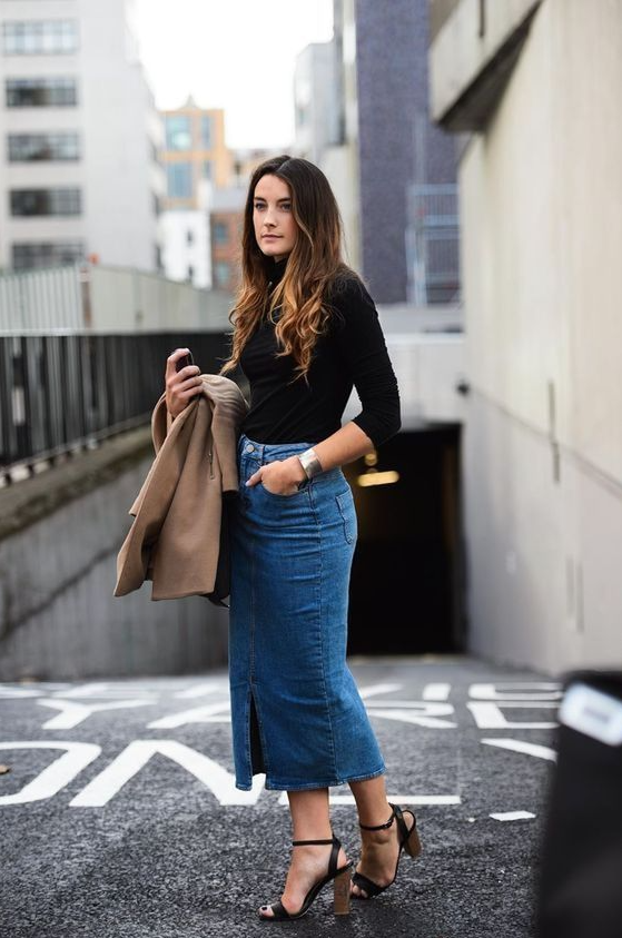 an elegant and simple look of a black turtleneck, a blue denim midi skirt with a front slit, black heels and a camel jacket