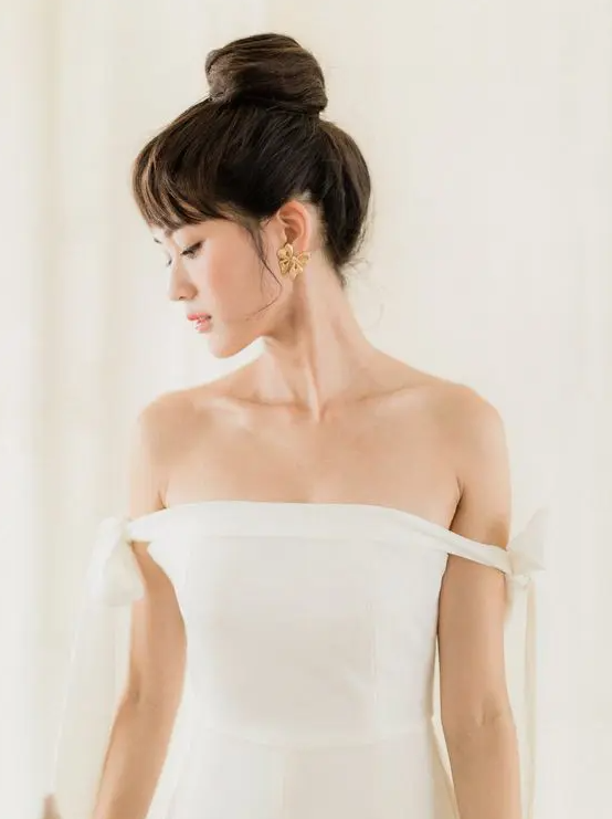 an elegant wedding top knot with a large wrapped knot and some volume plus a classic fringe is pure chic