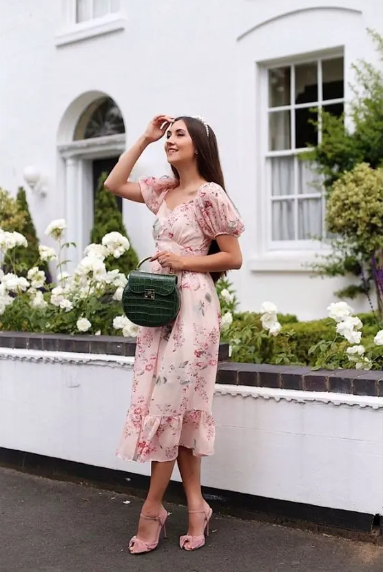 An eye catchy floral midi dress with puff sleeves, pink shoes and a green mini bag are a cute look for a spring wedding