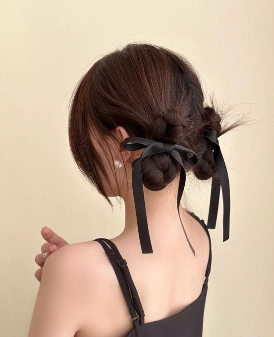 Low braided buns accented with black bows and with face framing bangs look super cute, girlish and lovely