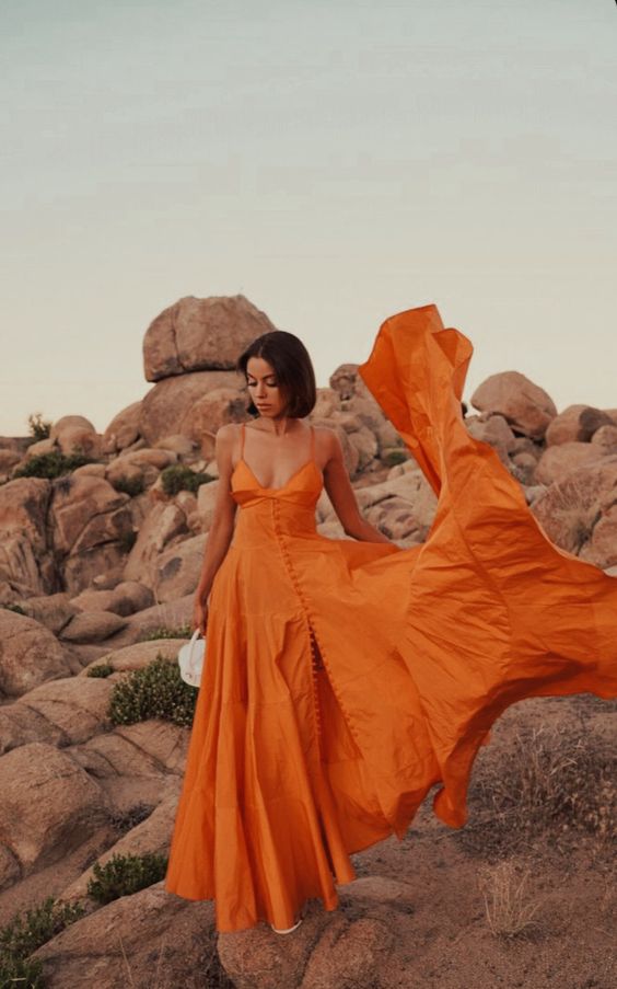 a bold orange maxi dress with spaghetti straps and buttons plus a small white bag and shoes are a cool combo for a beach wedding