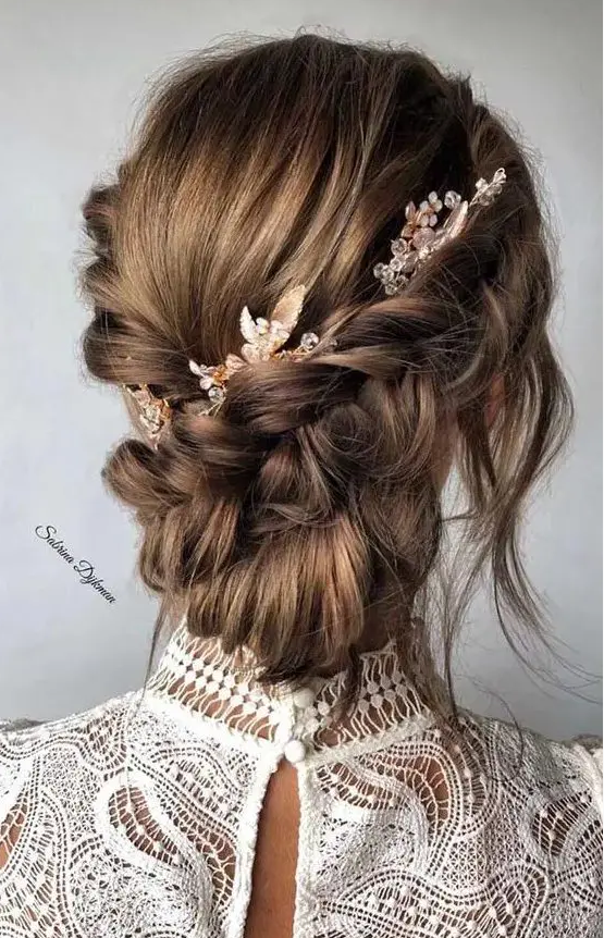 A braided low updo with two side braids, a bump, a low bun and face framing locks plus some beaded hair pieces