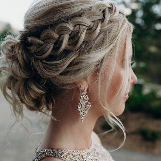 A braided updo with a bump on top and a messy low bun plus some face framing bangs is a chic wedding hairstyle