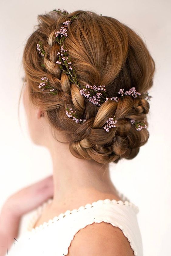 a braided updo with some fresh pink blooms tucked in is a cool hairstyle for a wedding, it looks chic and cool