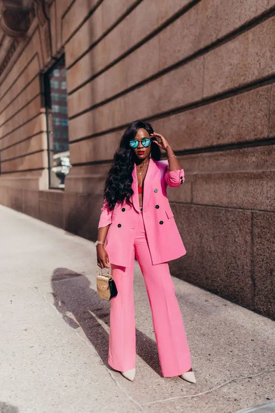 a bright pink power suit with an oversized blazer, white shoes, a small bag and a hot pink crop top underneath the blazer