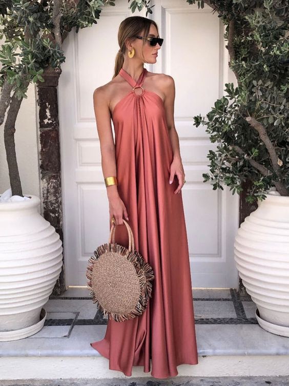 a burnt orange maxi dress with pleating and a loop on the neck, statement accessories and a woven bag for a tropical or beach wedding