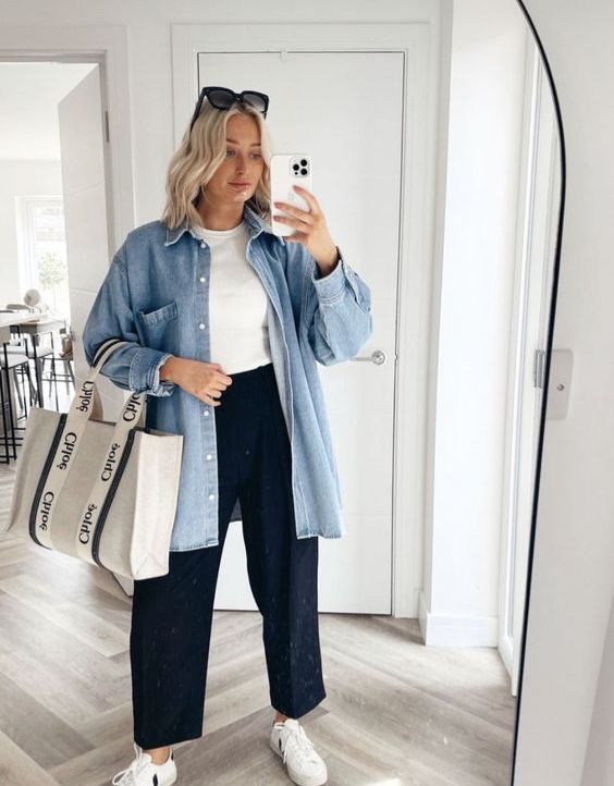 A classy and comfy outfit with a white t shirt, navy pants, an oversized blue denim shirt, a neutral tote and white sneakers