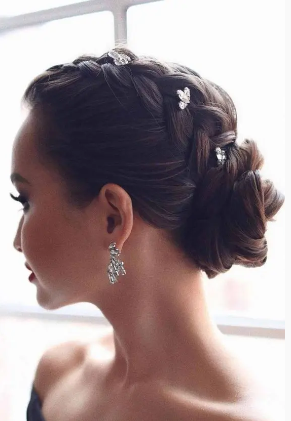 a glam updo with a braid on top and a low bun accented with rhinestone hairpins is a cool and catchy idea or a bride