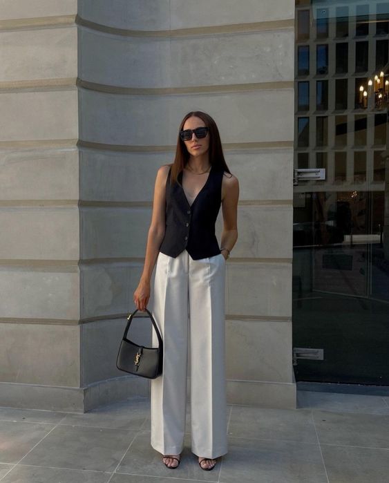 a laconic and modern graduation look with a black vest, white trousers, black shoes, a small baguette bag and a necklace is an outfit that always works