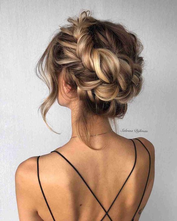 A lush and loose braided updo with a bump on top and face frmaing hair is a cool hairstyle for a wedding