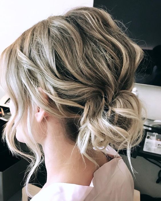 a messy and textural wavy bun with a bump on top and some face-framing hair is a cool hairstyle for a wedding