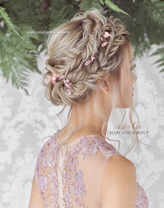 a messy braided updo with fishtail braids and pink blooms plus face framing bangs is a cool hairstyle to rock