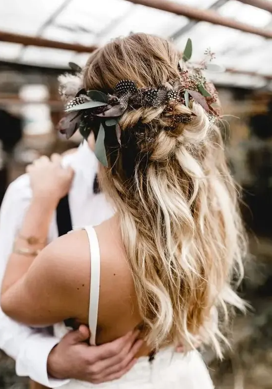 a messy textural half updo with twists and braids and greenery and feathers is ideal for a boho bride