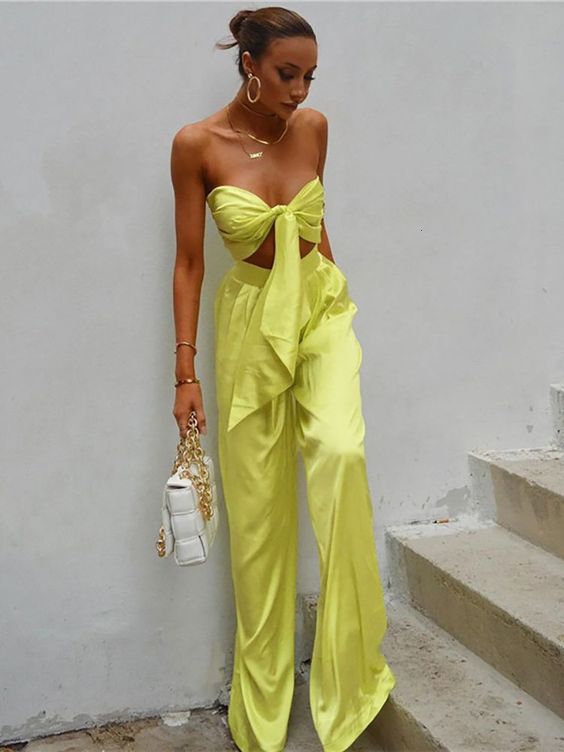 a neon yellow knotted crop top and matching high waisted pants, a white bag and gold jewelry for a modern beach wedding