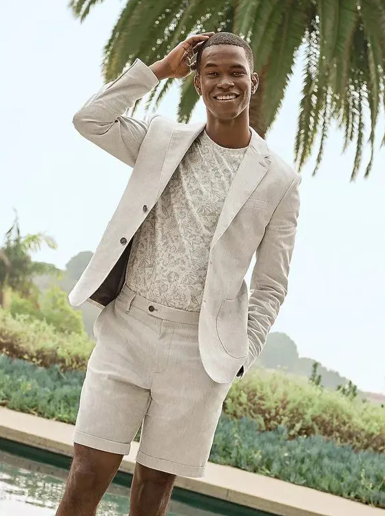 A neutral beach wedding guest look with a printed t shirt and a linen suit with shorts