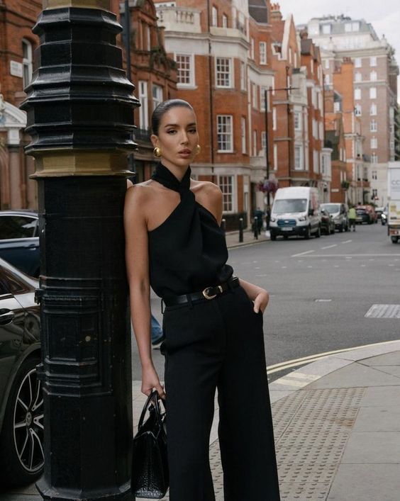 a refined total black look with a halter neck top with a loop on the neck, black pants, a black belt with a gold buckle, a black bag and chic gold earrings