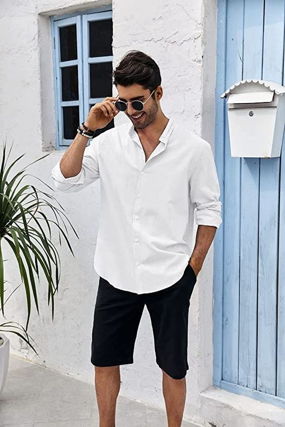 a relaxed beach wedding guest look with a white button down, black shorts, bracelets and sunglasses is cool