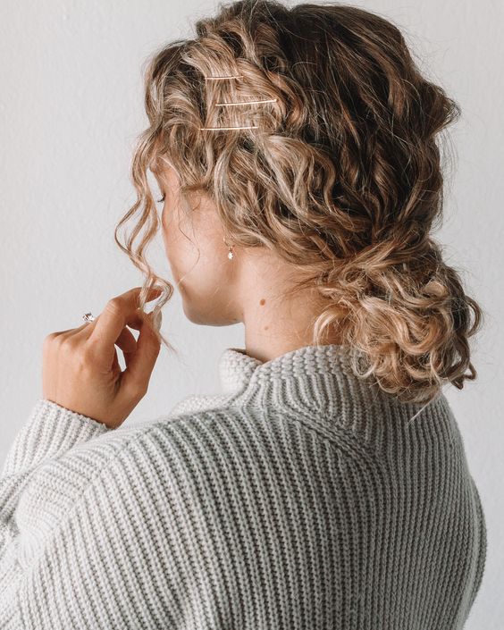 a simple messy low bun on curly hair, with face-framing locks and hairpins is a cool solution you can realize on the go