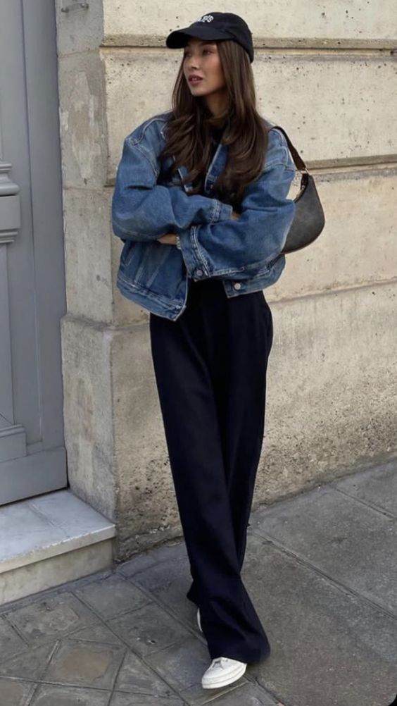 a spring look with a black top, black pants, white sneakers, a blue oversized denim jacket, a black baguette bag and a cap
