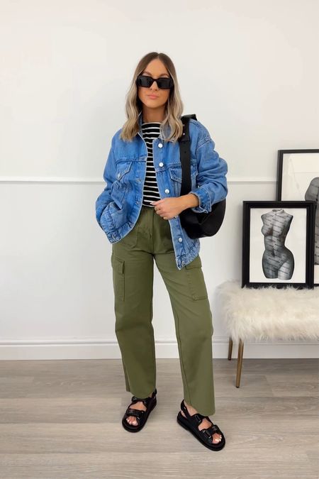 A spring look with a striped t shirt, a blue denim jacket, green cargo pants, black sandals and a black bag