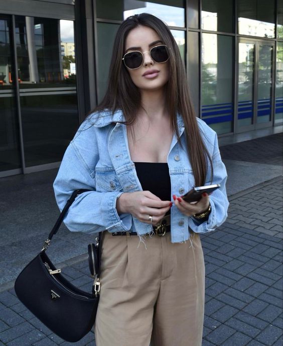a spring outfit with a black top, tan pants, a bleached cropped denim jacket and a black baguette bag
