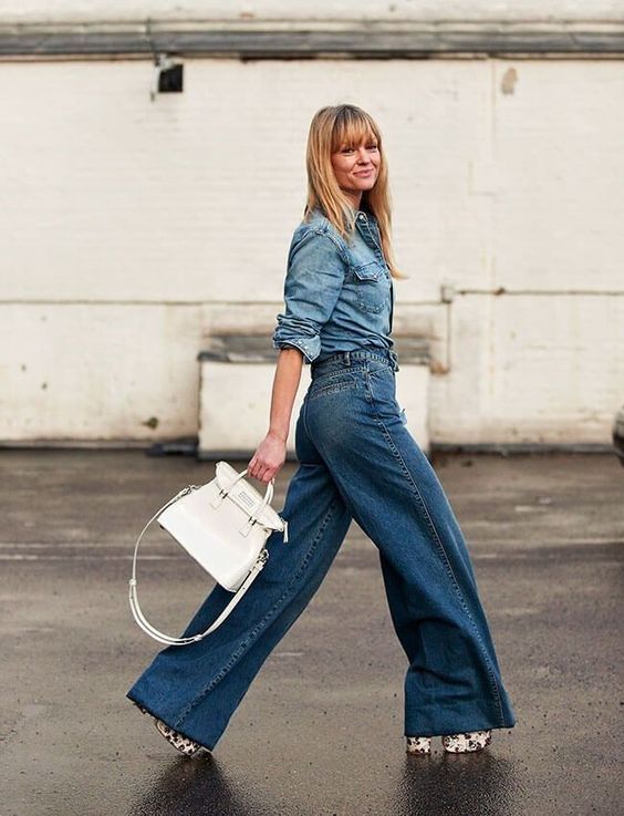 a spring outfit with a blue denim shirt, wideleg jeans, printed platform shoes and a white bag is bold and trendy