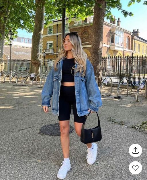 a spring to summer look with a black top and bike shorts, an oversized blue denim jacket, white trainers and a black baguette bag
