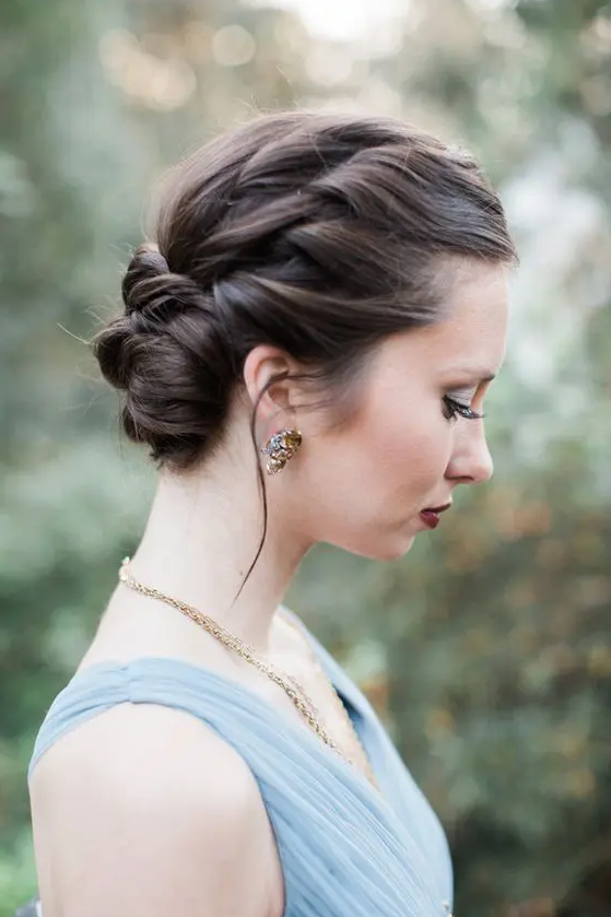a stylish braided halo updo with a low bun and volume on top is a cool and chic idea for a wedding