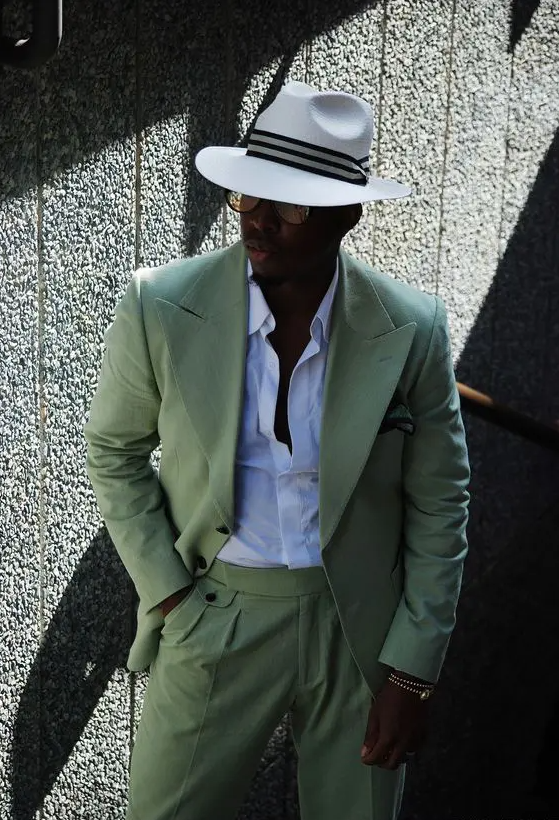 a super elegant beach wedding guest look with a white shirt, a green pantsuit and a hat with a ribbon plus sunglasses