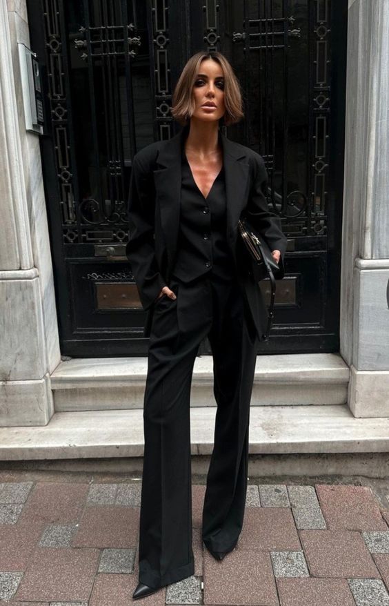a total black outfit with a three-piece pantsuit, flare pants, pointed toe shoes and a small vintage-inspired bag