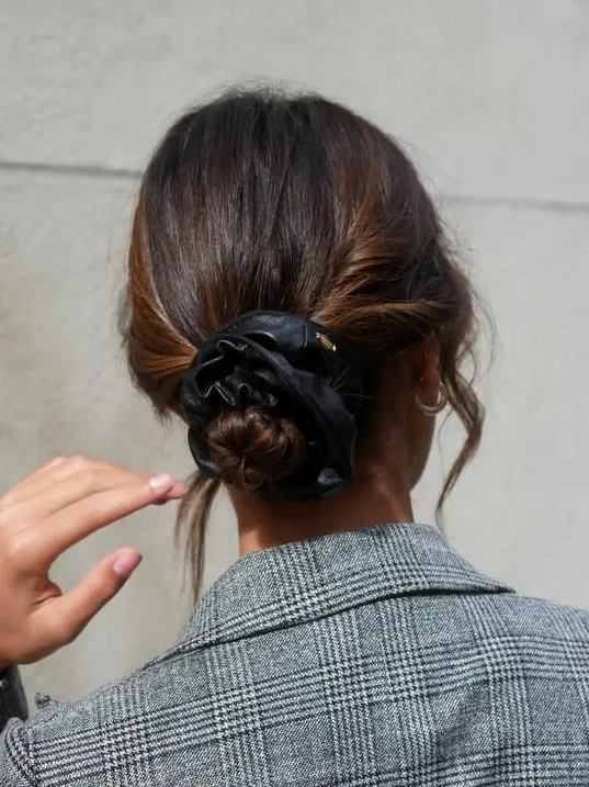 a twisted low bun with face-framing hair and a black elather scrunchie is a lovely hairstyle to rock