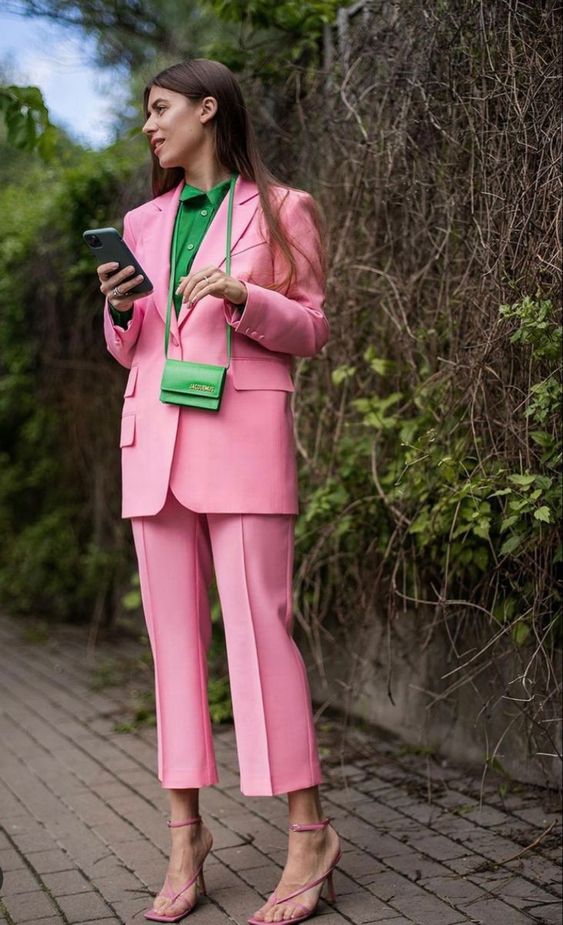 a whimsical and colorful outfit with a pink pantsuit with cropped pants, a green button down, a green bag and pink strappy shoes
