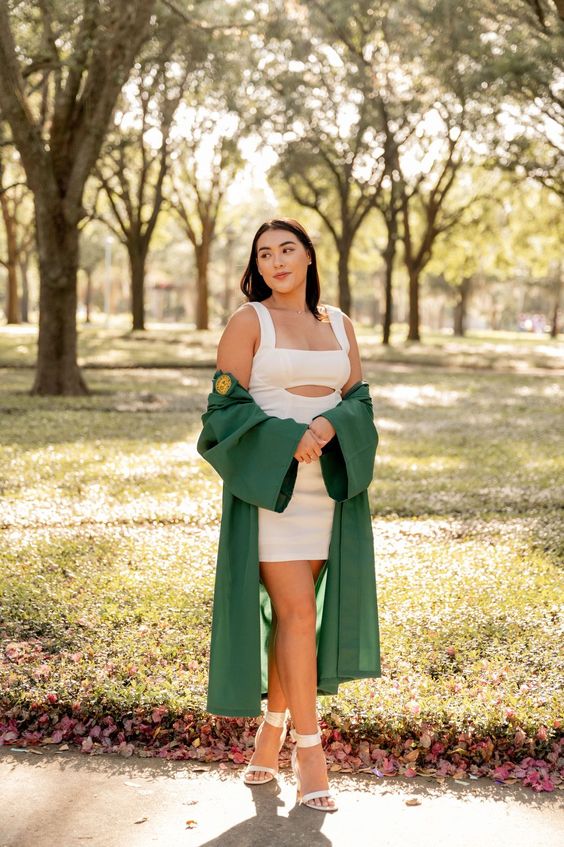 a white bodycon mini dress with straps and a cutout, white ankle strap shoes and a green robe for a cool and sexy graduation look