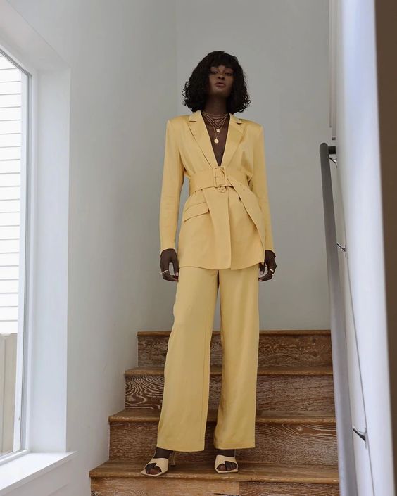 a yellow pantsuit with a belt, layered necklaces, nude shoes and chic rings is a cool idea for spring and summer weddings