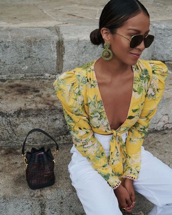 a yellow tropical print knotted crop top, white high waisted linen pants, a small bag and statement earrings
