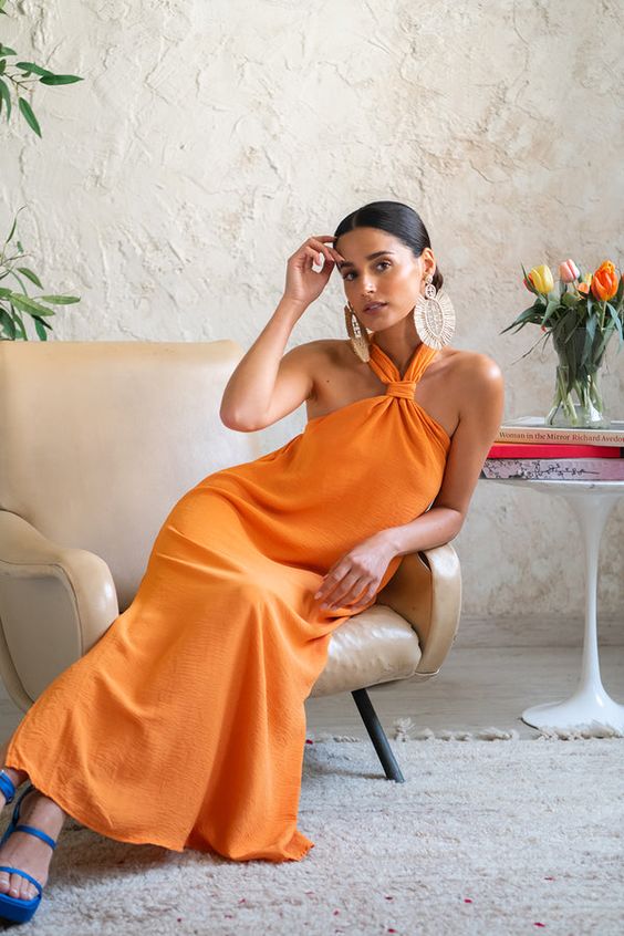 an orange maxi dress with a loop on the neck, bold blue platform shoes and statement earrings are a lovely combo for a beach wedding