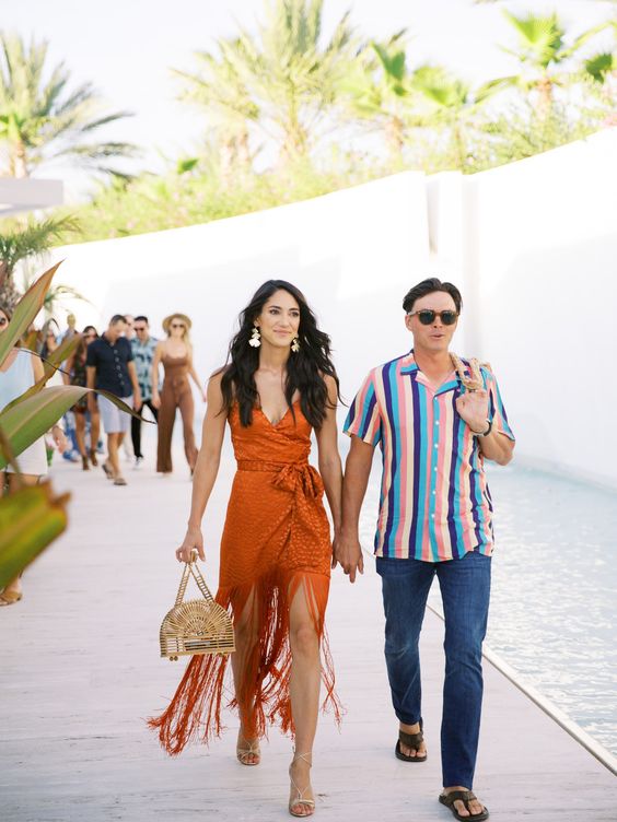 an orange over the knee dress with long fringe, statement earrings and a wooden bag are a chic combo for a beach wedding