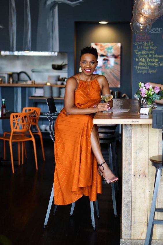 an orange striped halter neckline maxi dress, clear shoes and statement earrings are a bold and cool look